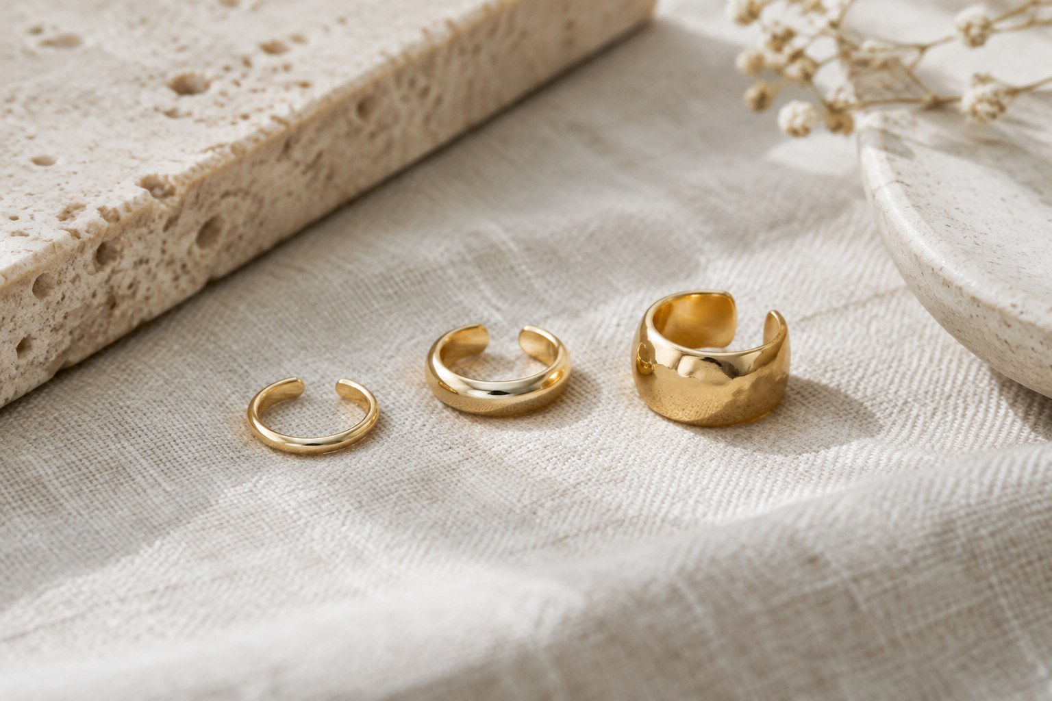 Illustration: three gold ear cuffs of different widths on linen