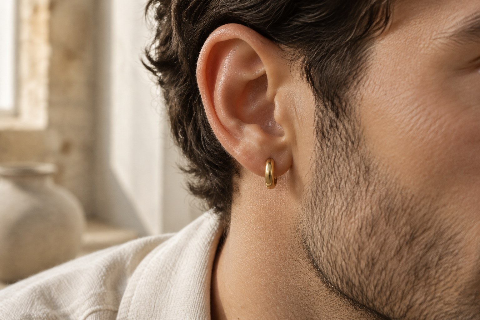 A man's ear wearing a small gold huggie hoop