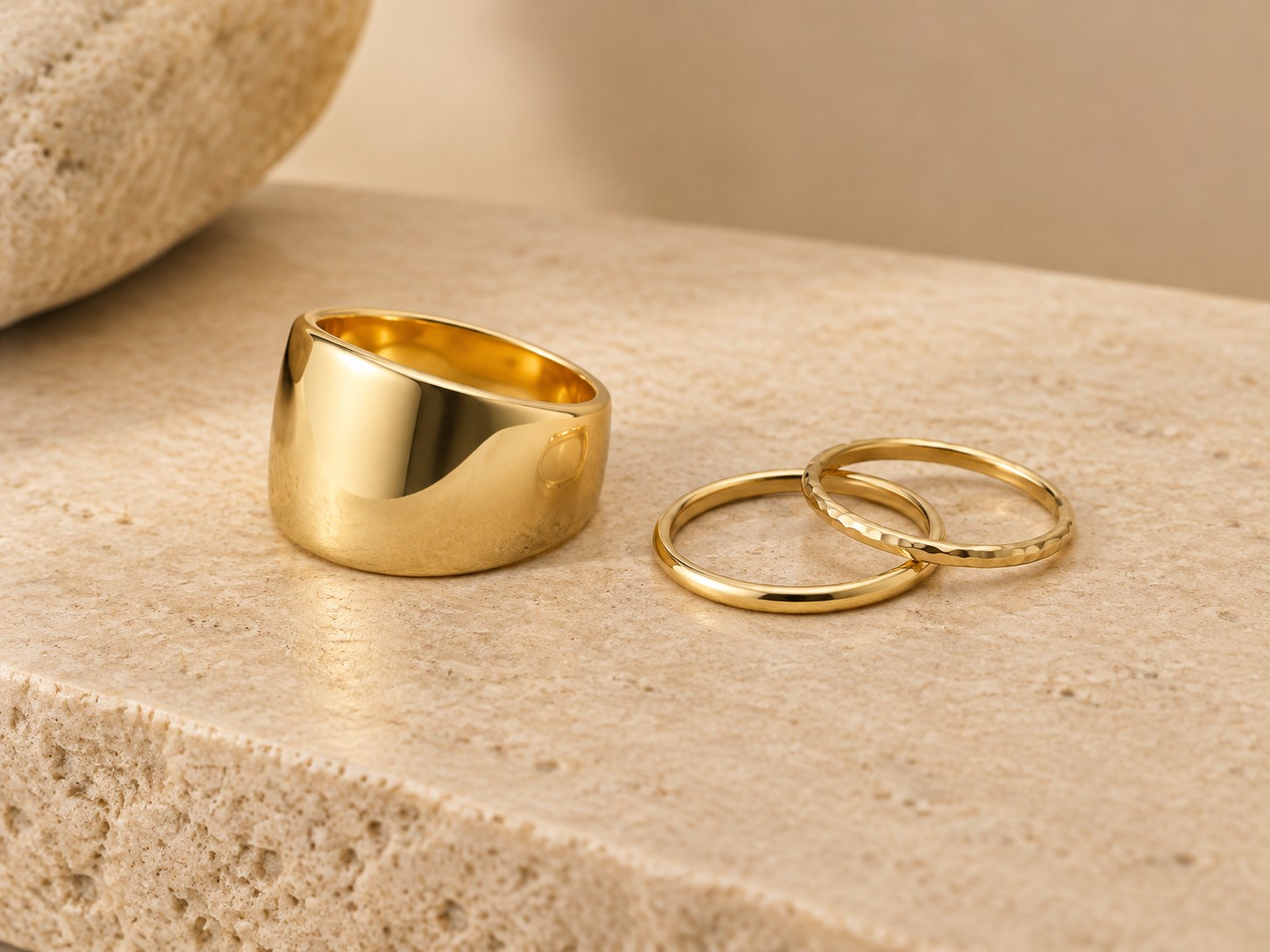 AI illustration of a wide modern gold thumb ring beside slim stacking bands.