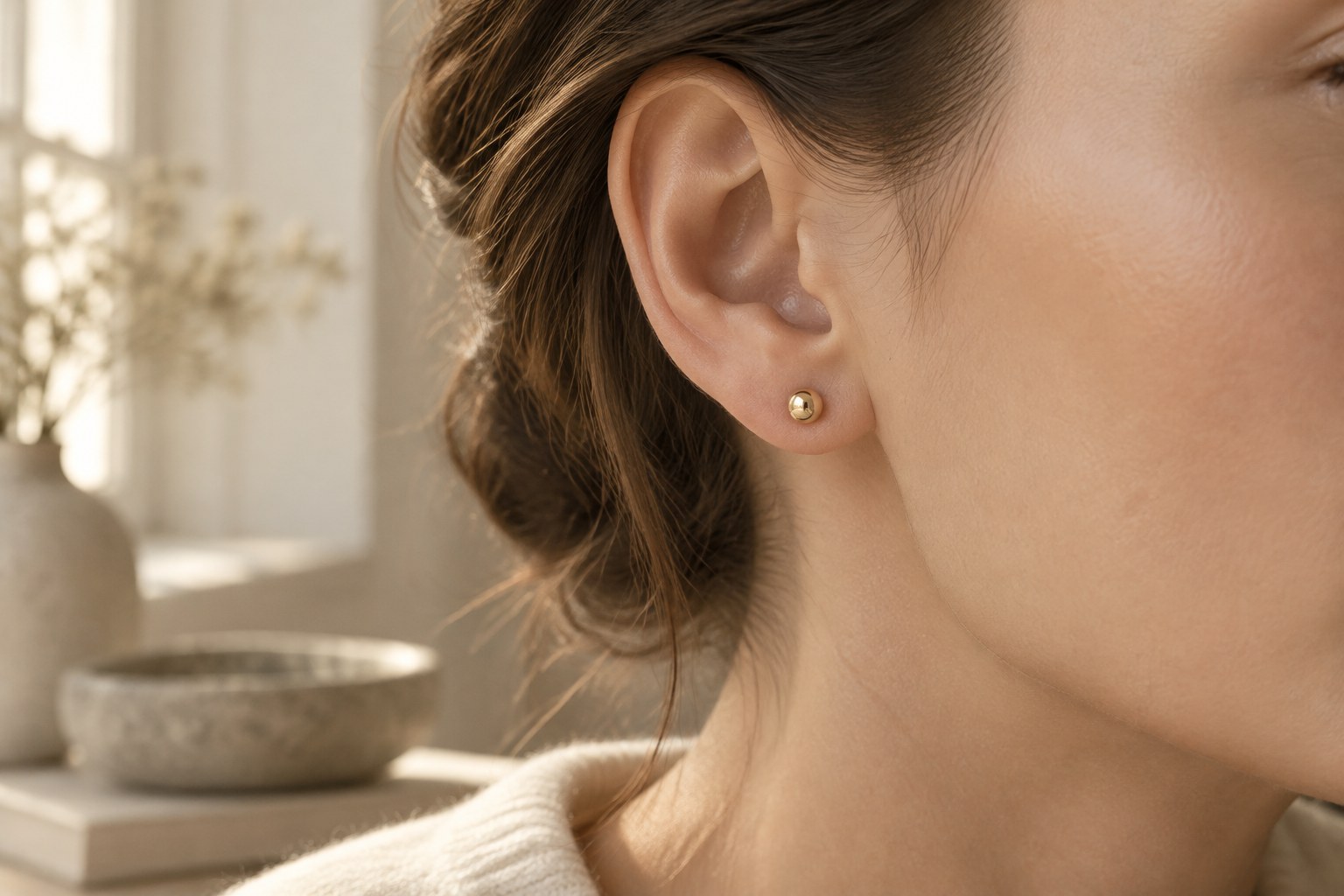 A woman's ear wearing a small solid gold stud