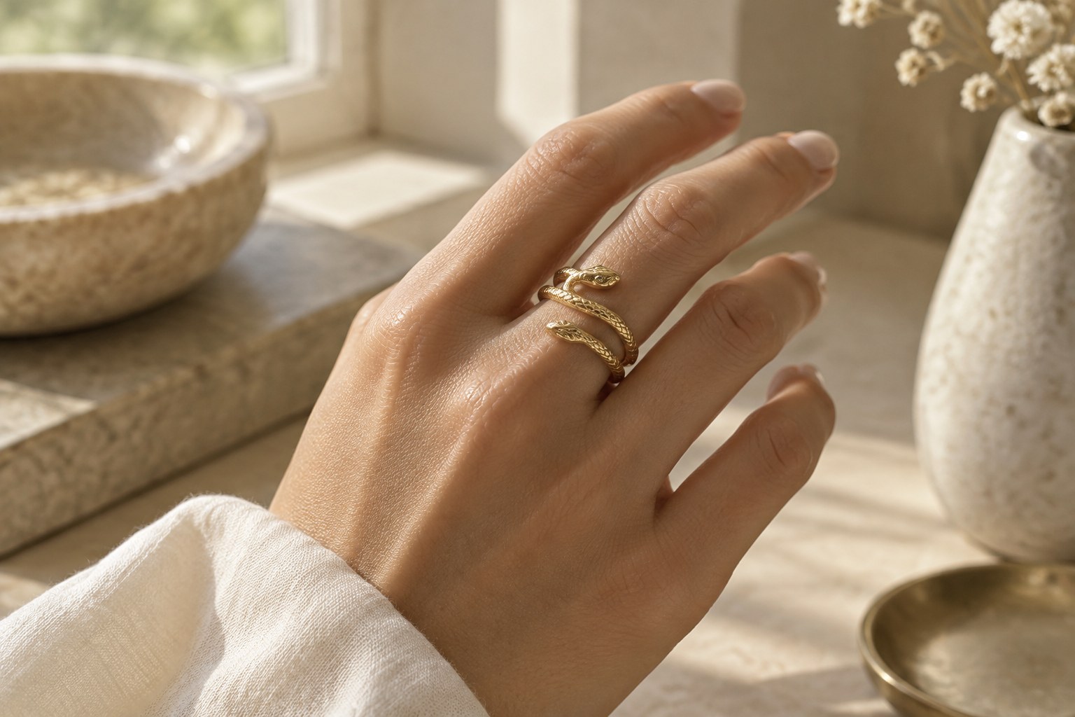 A hand wearing a delicate gold serpent ring in soft light