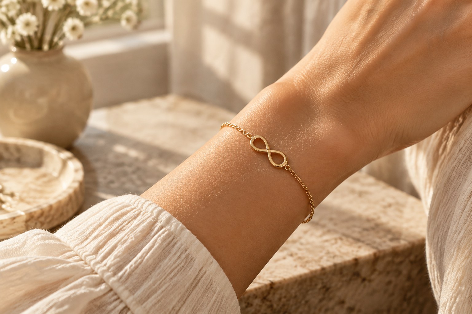 A wrist wearing a delicate gold infinity bracelet in sunlight